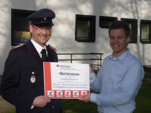 Sportbeauftragter Harald Sinske (FF Gülzow, li.) nimmt freudestrahlend den Sportgutschein von Jens-Oliver Mohr (HFUK Nord, re.) entgegen.