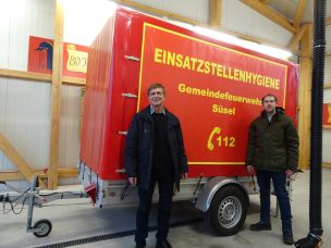 Gemeindewehrführer Rolf Müller (links) und Sascha Struck von der FF Röbel führen den Anhänger "Einsatzstellenhygiene" vor. (Bild: Christian Heinz / HFUK Nord)