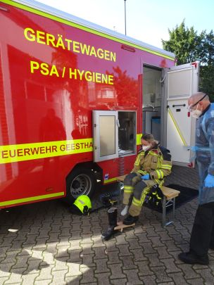 Katharina von Goeckingk von der FF Geesthaht zeigt die Funktionsweise des GW PSA/Hygiene: Eine Grobreinigung und das Ablegen von Helm und Stiefeln erfolgen draußen, danach geht es ins Fahrzeuginner in Einbahnstraßenprinzip. (Bild: Christian Heinz / HFUK Nord)